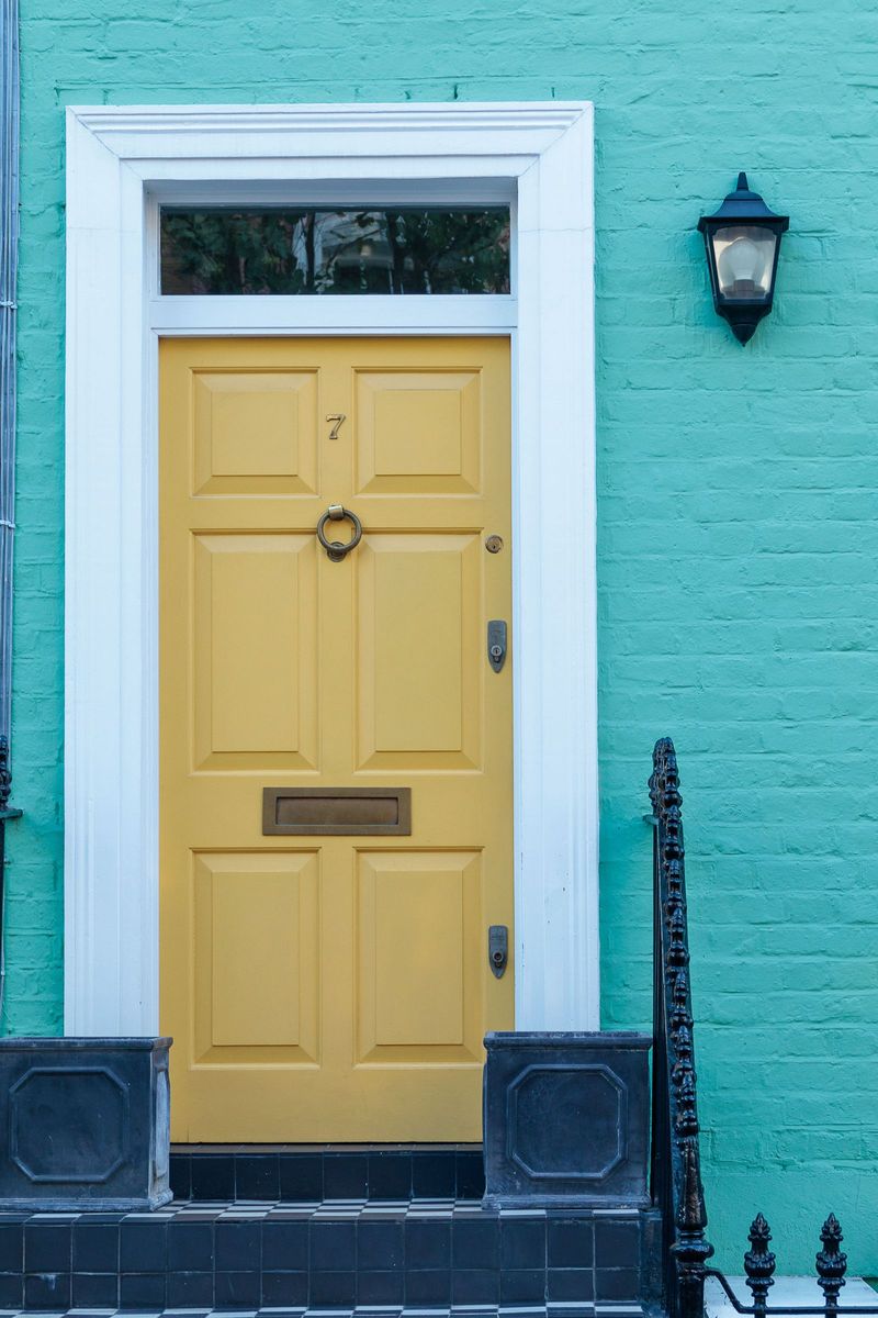 Yellow front door with white trim on a painted brick wall